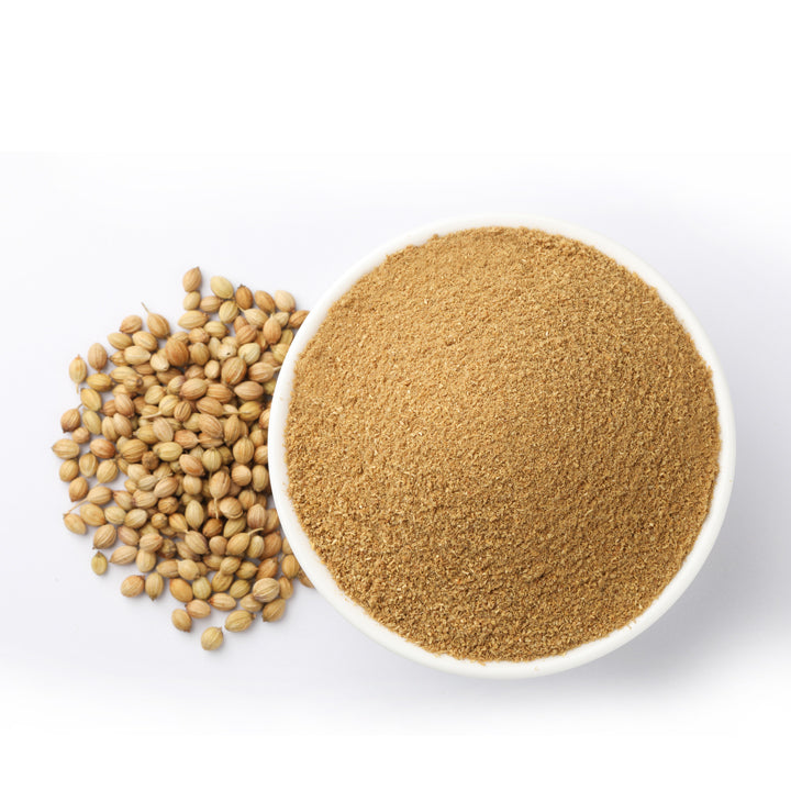 Coriander powder in a white bowl with whole coriander seeds beside it, showing the fresh homemade texture of Mantra Herbs natural spice.