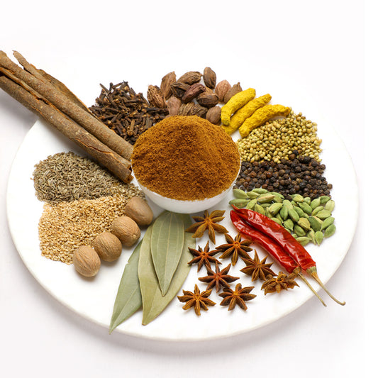 Garam masala powder in a bowl surrounded by whole spices like cinnamon, cloves, nutmeg, and cardamom, showing the natural homemade blend by Mantra Herbs.